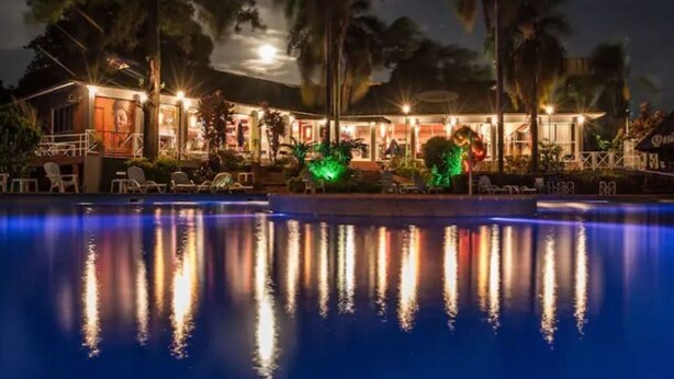 A nighttime view of a hotel with a swimming pool, palm trees, and illuminated outdoor seating areas. - Tangoinn Bed and Brewery (Puerto Iguazú)