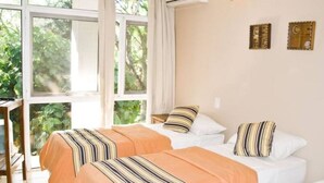 A hotel room with two beds, large windows, and a view of greenery outside. - Tangoinn Bed and Brewery (Puerto Iguazú)