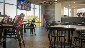 A modern restaurant with wooden chairs and tables, large windows, and a television displaying a news program.