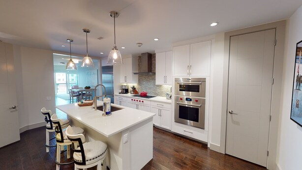 A modern kitchen with white cabinetry, stainless steel appliances, and pendant lighting.