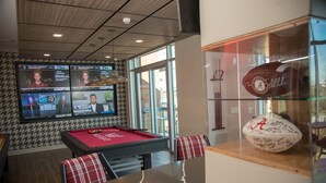 A billiards room with a pool table, multiple screens displaying sports content, and a glass display case with a signed football.