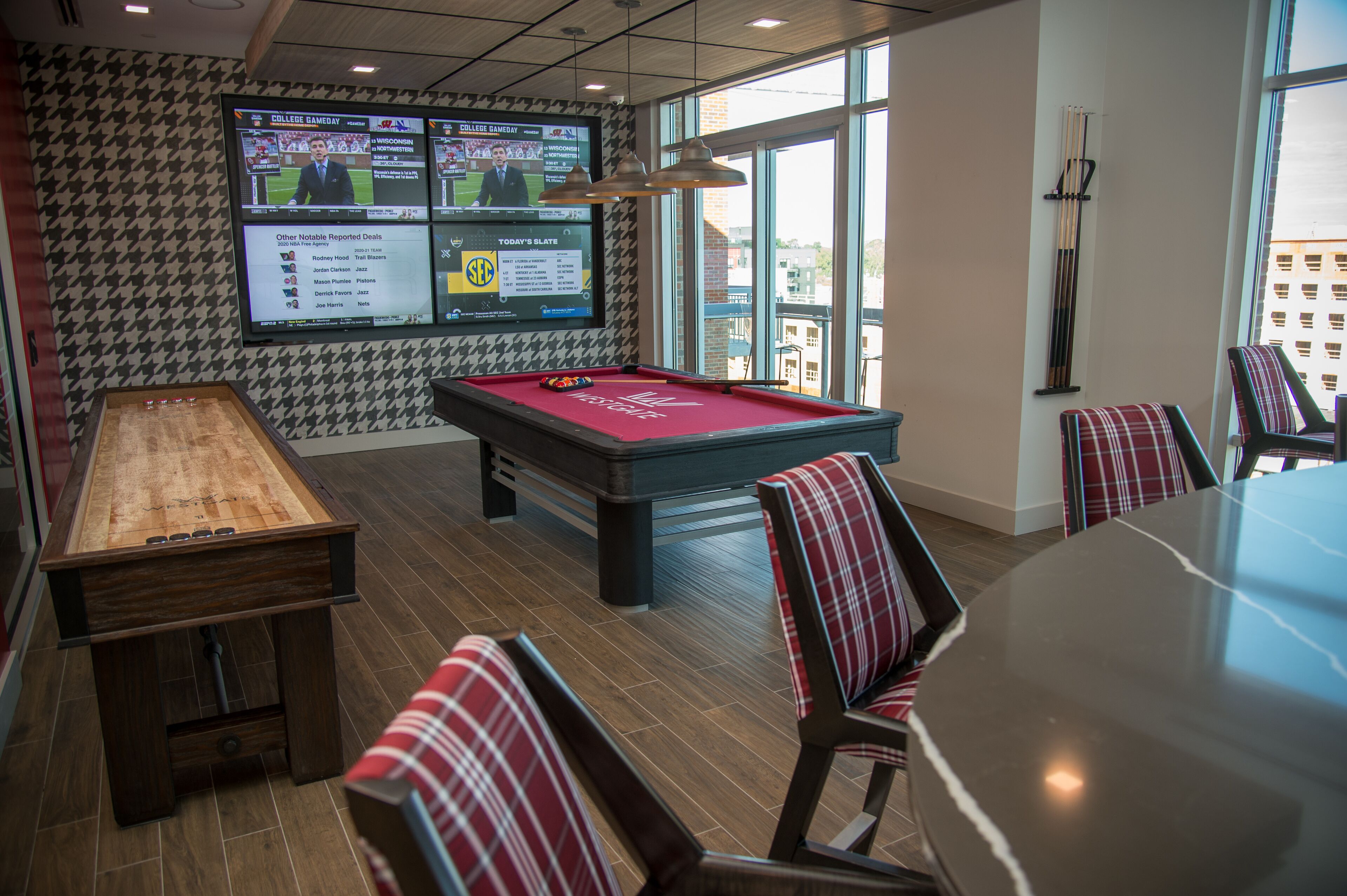 A billiards room with a pool table, chairs, and a television displaying sports.