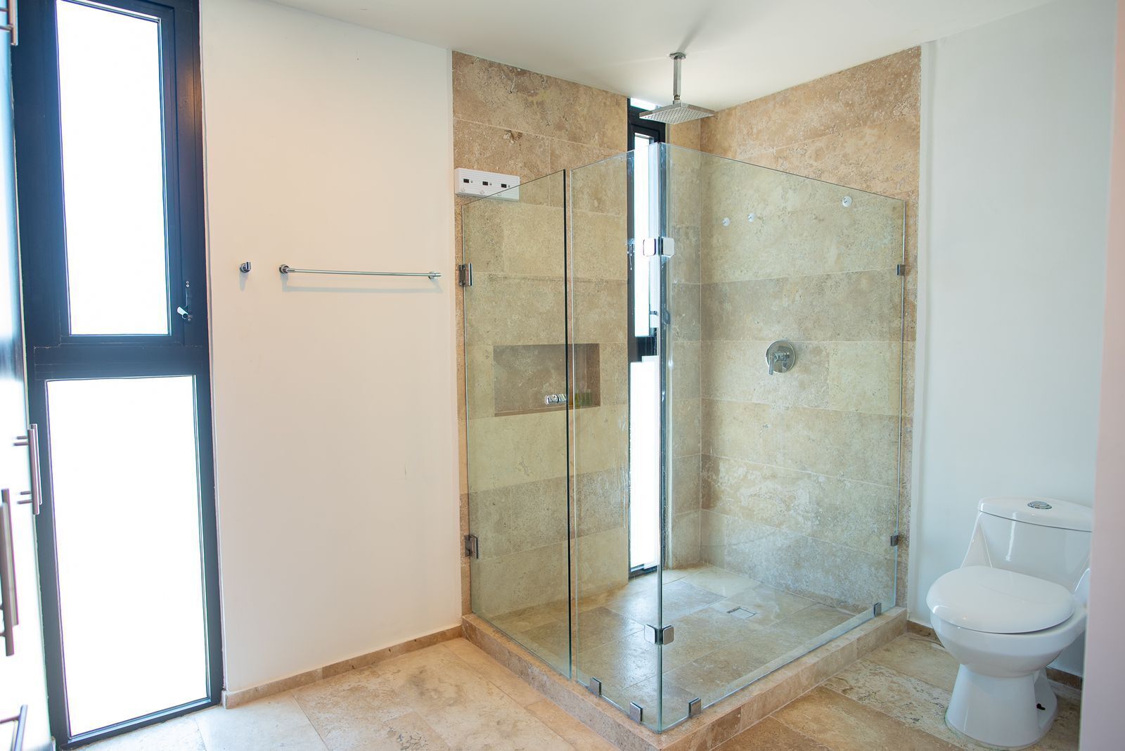 Une salle de bain moderne avec une douche à parois de verre, des toilettes et une porte donnant sur une autre pièce.