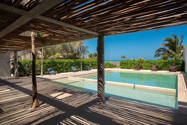 A pool area with lounge chairs and a view of the ocean.