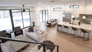 A modern kitchen with a central island, bar stools, and a dining area with a long table. - Luxury New Build, Private Pool and Spa, Sleeps 10 all King, 4 min to Dt (Austin)