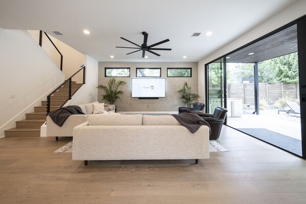 A spacious living room with a large sectional sofa, a staircase, and a modern ceiling fan.