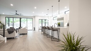 A modern kitchen with a bar area, large windows, and a staircase leading to an upper level. - Luxury New Build, Private Pool and Spa, Sleeps 10 all King, 4 min to Dt (Austin)