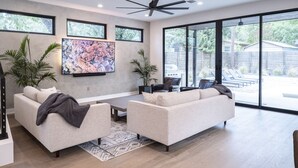 A modern living room with two sofas, a flat-screen TV, and a ceiling fan. - Luxury New Build, Private Pool and Spa, Sleeps 10 all King, 4 min to Dt (Austin)