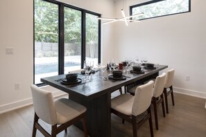 A dining area with a long table set for six, large windows, and a modern light fixture.