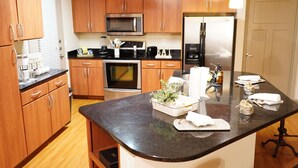 A modern kitchen with wooden cabinets, a microwave, an oven, a refrigerator, and a central island with a plant and napkins. - The Tranquility Den (NRG,City Centre, Galleria) (Houston)
