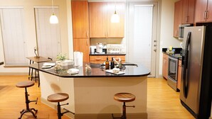 A modern kitchen with wooden cabinets, a stainless steel refrigerator, and a central island with stools. - The Tranquility Den (NRG,City Centre, Galleria) (Houston)