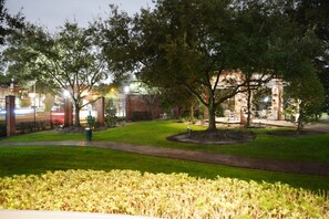 Stroll through the serene grounds, surrounded by lush trees and a manicured lawn, leading to a charming building with a brick facade.