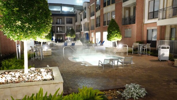 An outdoor pool area with lounge chairs and a fire pit, surrounded by a brick building with balconies. - The Tranquility Den (NRG,City Centre, Galleria) (Houston)