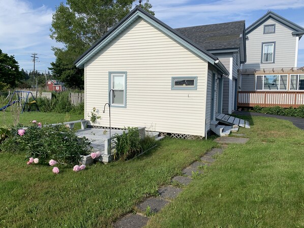 Ein Bungalow mit einer kleinen Veranda und einem Garten mit rosa Blumen.