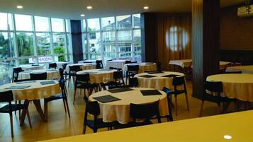 A dining area with round tables and chairs, large windows with a view, and a sign that reads "NAZAI".