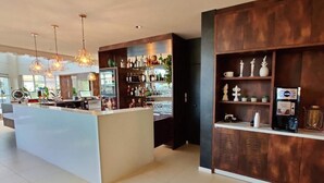 Zona de bar moderna con una isla central, iluminación colgante y una variedad de botellas y vasos en estantes.