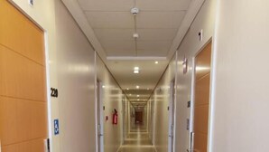 Un largo y estrecho pasillo de hotel con puertas de madera a ambos lados, placas con números de habitación y un extintor en la pared.
