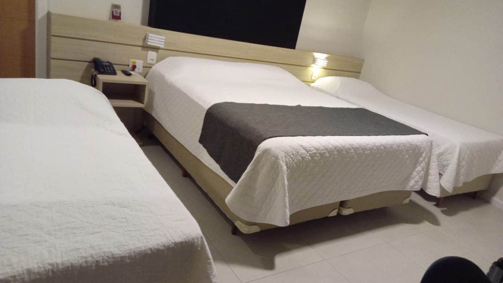 Una habitación de hotel con dos camas individuales, una mesita de noche con teléfono, una lámpara y un televisor montado en la pared.