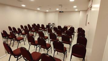 A conference room with rows of red chairs, a projector screen, and a table with chairs.