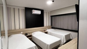Habitación de hotel con dos camas individuales, un escritorio, una silla, un televisor y un equipo de aire acondicionado.
