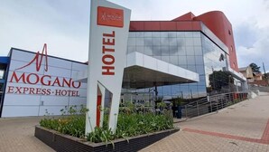 Exterior del Hotel Mogano Express, con un letrero llamativo, arquitectura moderna y un área ajardinada en la parte frontal.