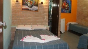 A hotel room with a brick wall, a bed with a blue bedspread, two bedside tables, a painting of flowers, and an orange accent wall. - Pousada Raja Canto do Mar (Ipojuca)