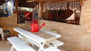 An outdoor patio with a white table and benches, a red watering can, and a brick wall. - Pousada Raja Canto do Mar (Ipojuca)