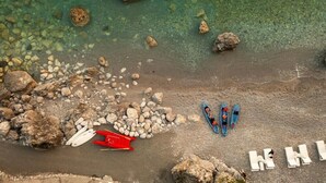 Ovenfra set strand med sten, et rødt paddleboard og en blå kajak.