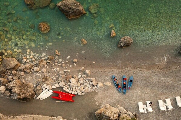 Vista aérea de una playa con rocas, una tabla de paddle surf roja y un kayak azul.