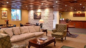 A hotel lobby with a wooden ceiling, a stone wall, a reception desk, a sofa, a chair, and a coffee table. - Hotel El Paraiso (Mineral del Chico)