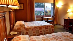 A hotel room with two beds, a small table, a chair, and a window with curtains. - Hotel El Paraiso (Mineral del Chico)