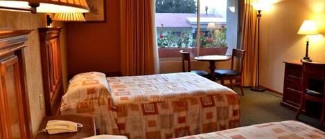 A hotel room with two beds, a small table, a chair, and a window with curtains.