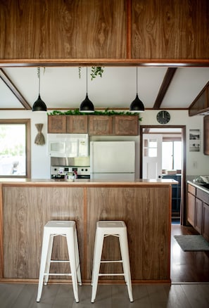 A kitchen with wooden cabinets, a central island with stools, a microwave, stove, and hanging pendant lights.