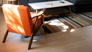 Un salon avec un canapé de couleur foncée, une table basse blanche et un tapis à rayures. On y trouve une lampe, un fauteuil et un ventilateur de plafond.