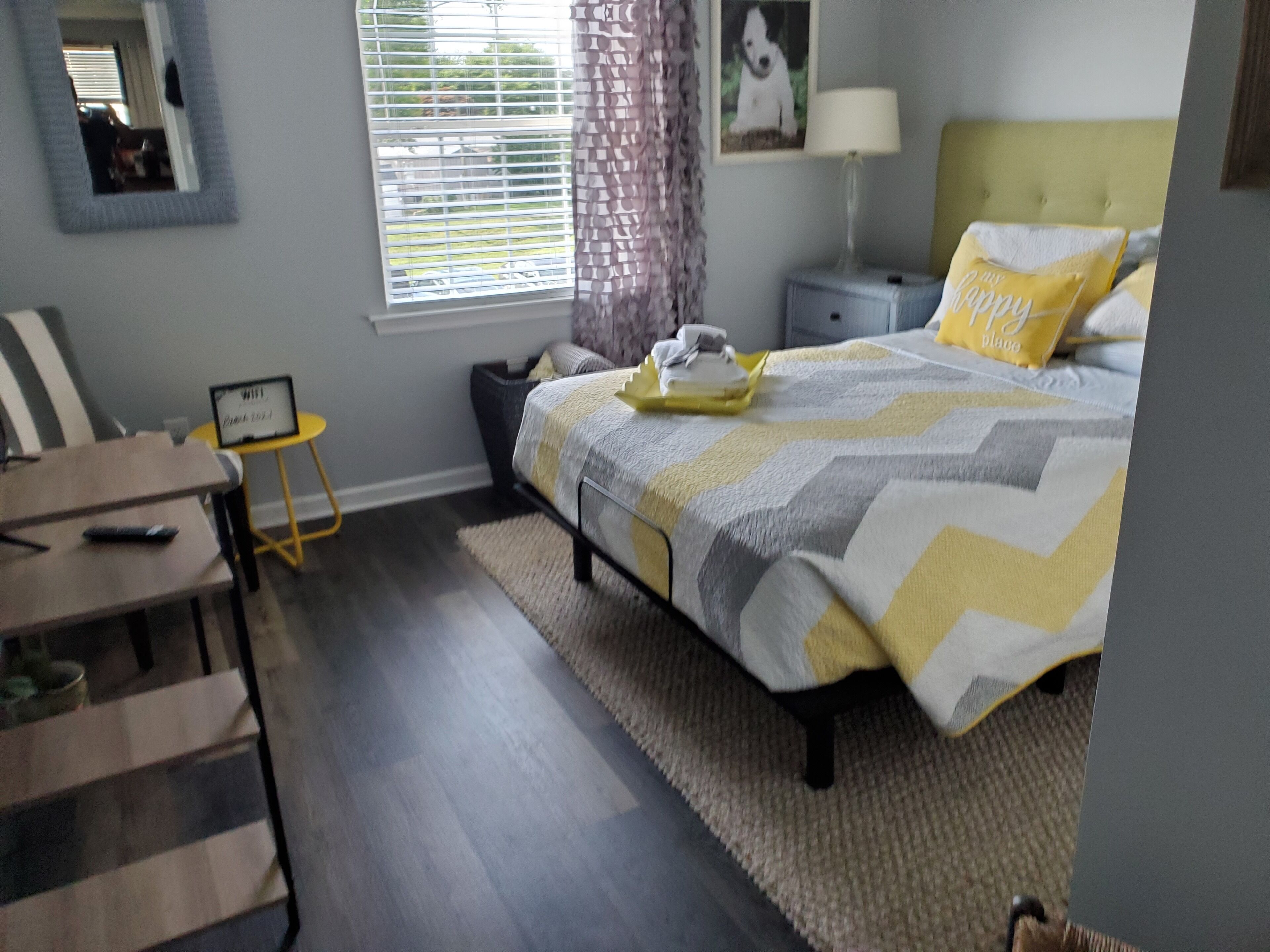 A bedroom with a bed, bedside table, lamp, and a small table with a chair.
