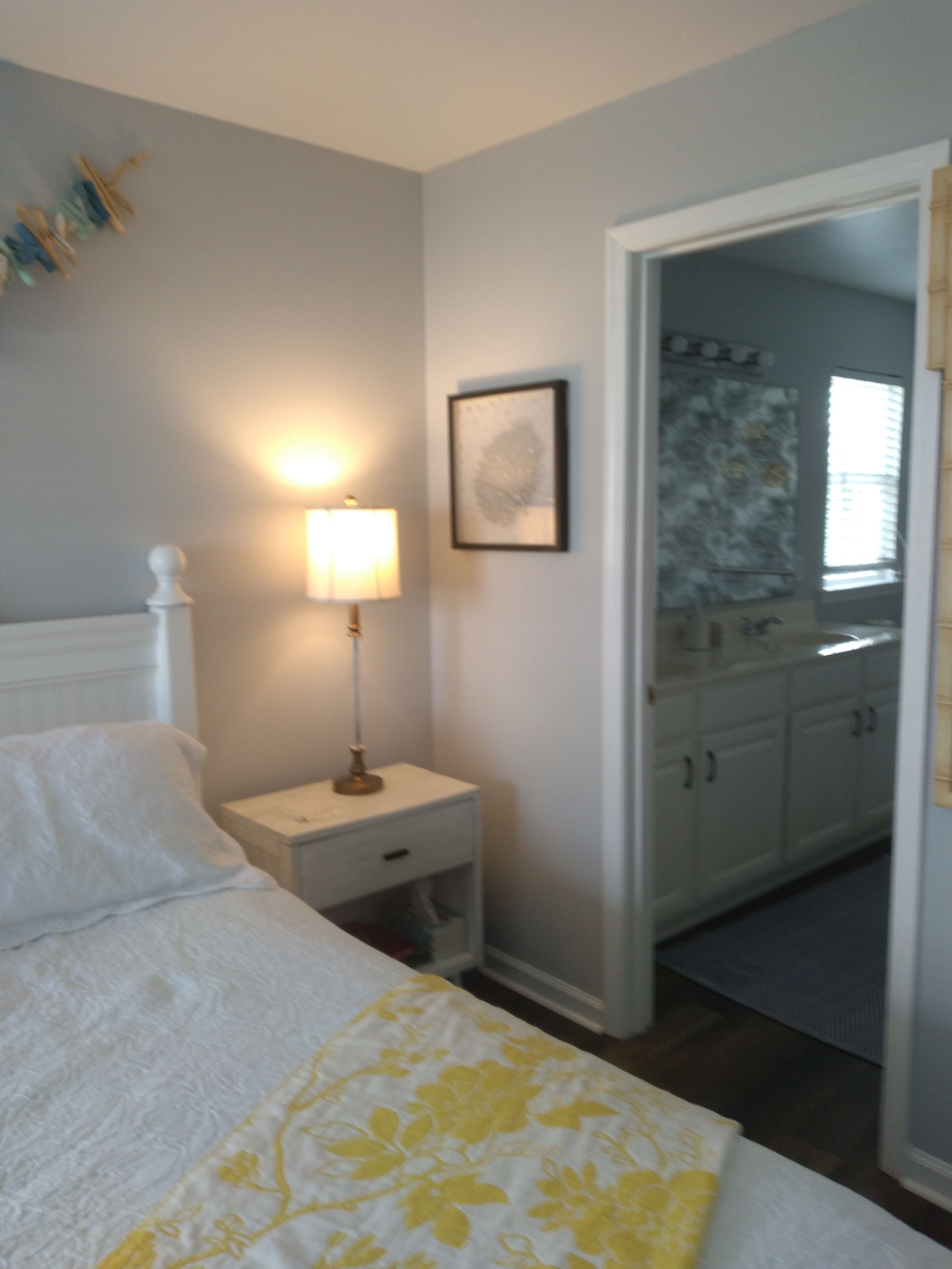 A bedroom with a bed, bedside table, lamp, and a mirror.