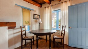 Een eethoek met een ronde tafel en twee stoelen, een lamp, een raam met gordijnen, en een blauwe deur.