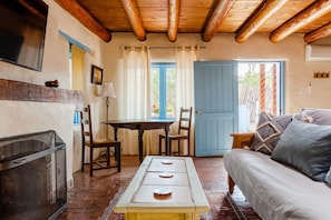 A cozy room with a fireplace, a wooden ceiling, a dining table with chairs, a sofa, and a door leading outside.