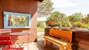 Een terras met een houten bank, rode stoelen en een tafel.