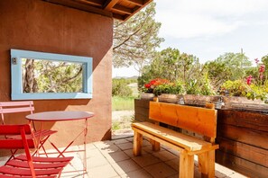 A patio with a wooden bench, red chairs, and a table.