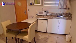 Cocina compacta con microondas, refrigerador pequeño y lavamanos. Hay una mesa de comedor con sillas.