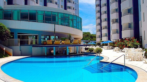 Un hotel moderno con piscina, varios balcones y zonas de estar al aire libre.