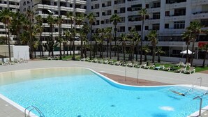 A swimming pool with a curved edge, surrounded by lounge chairs and palm trees. - Lighthouse Friendly Holiday Home (Playa del Inglés)