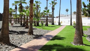 A pathway lined with palm trees and a grassy area, leading to a white building with a flat roof. - Lighthouse Friendly Holiday Home (Playa del Inglés)