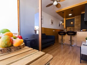 En moderne stue med sofa, to barstole, et træbord og en loftventilator.
