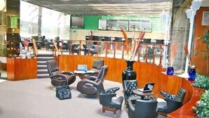Un hall con mostrador de recepción, zona de estar con sillas y sofás, y una escalera que lleva a un nivel superior.