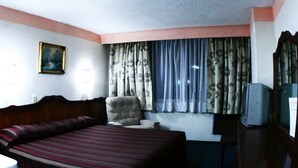 Una habitación de hotel con una cama grande, una silla, un televisor y un cuadro en la pared.