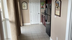 A hallway with a white door, beige walls, and a tiled floor. There is a refrigerator and a microwave on the right side. - Lake House with stunning view of Lake Cumberland (Somerset)