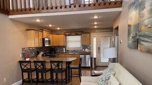 A modern kitchen with wooden cabinets, a central island with bar stools, a dining table, and a living area with a sofa and a glass coffee table. - Lake House with stunning view of Lake Cumberland (Somerset)