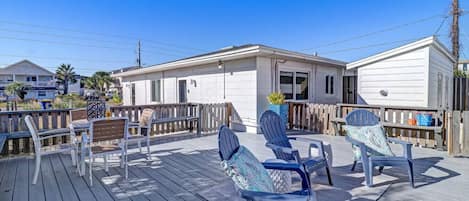 A deck with outdoor seating, a white building, and a wooden fence.